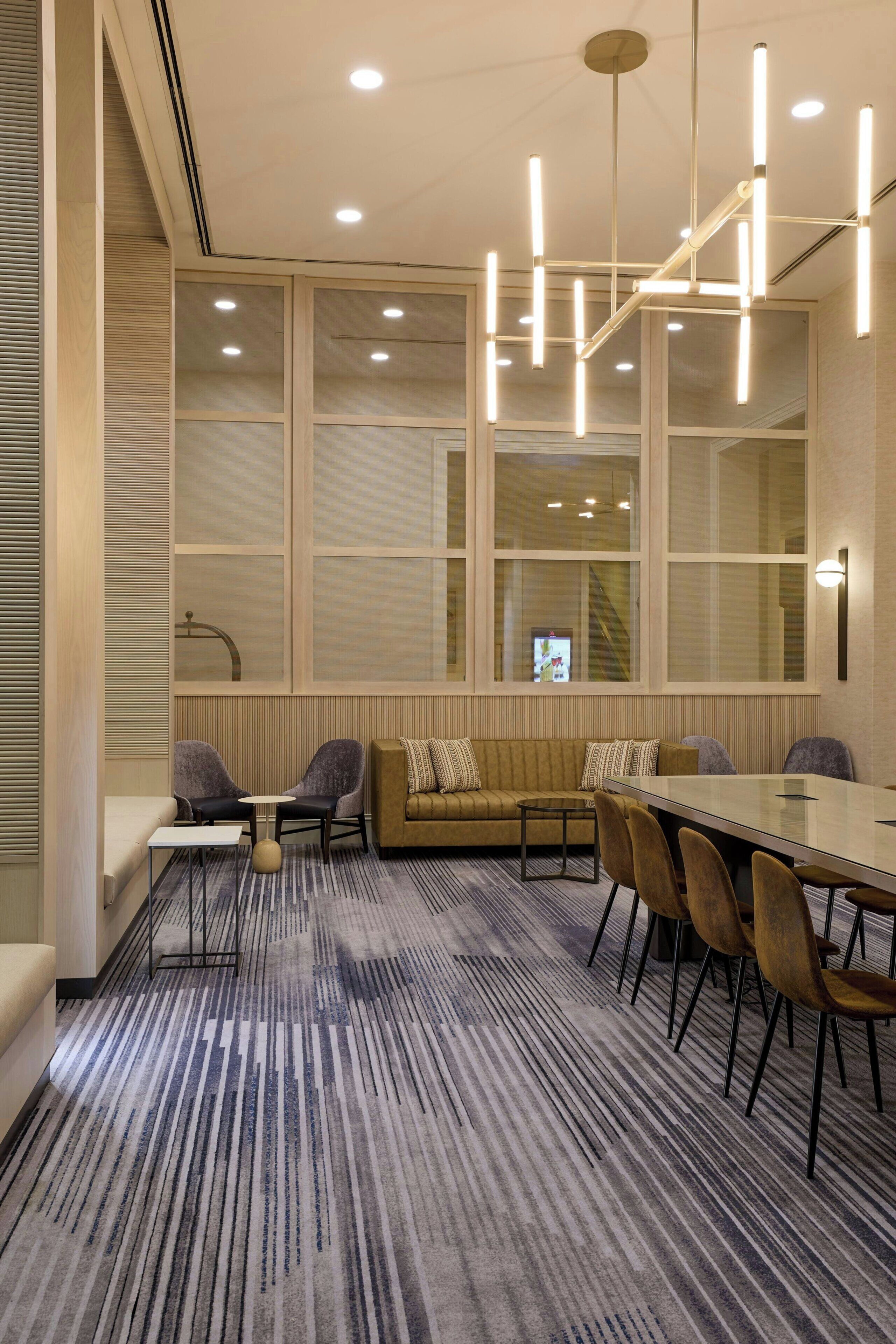A modern conference room with a long table, chairs, a sofa, and a large window with blinds.