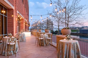 Un patio al aire libre con mesas y sillas, luces colgantes y macetas grandes.