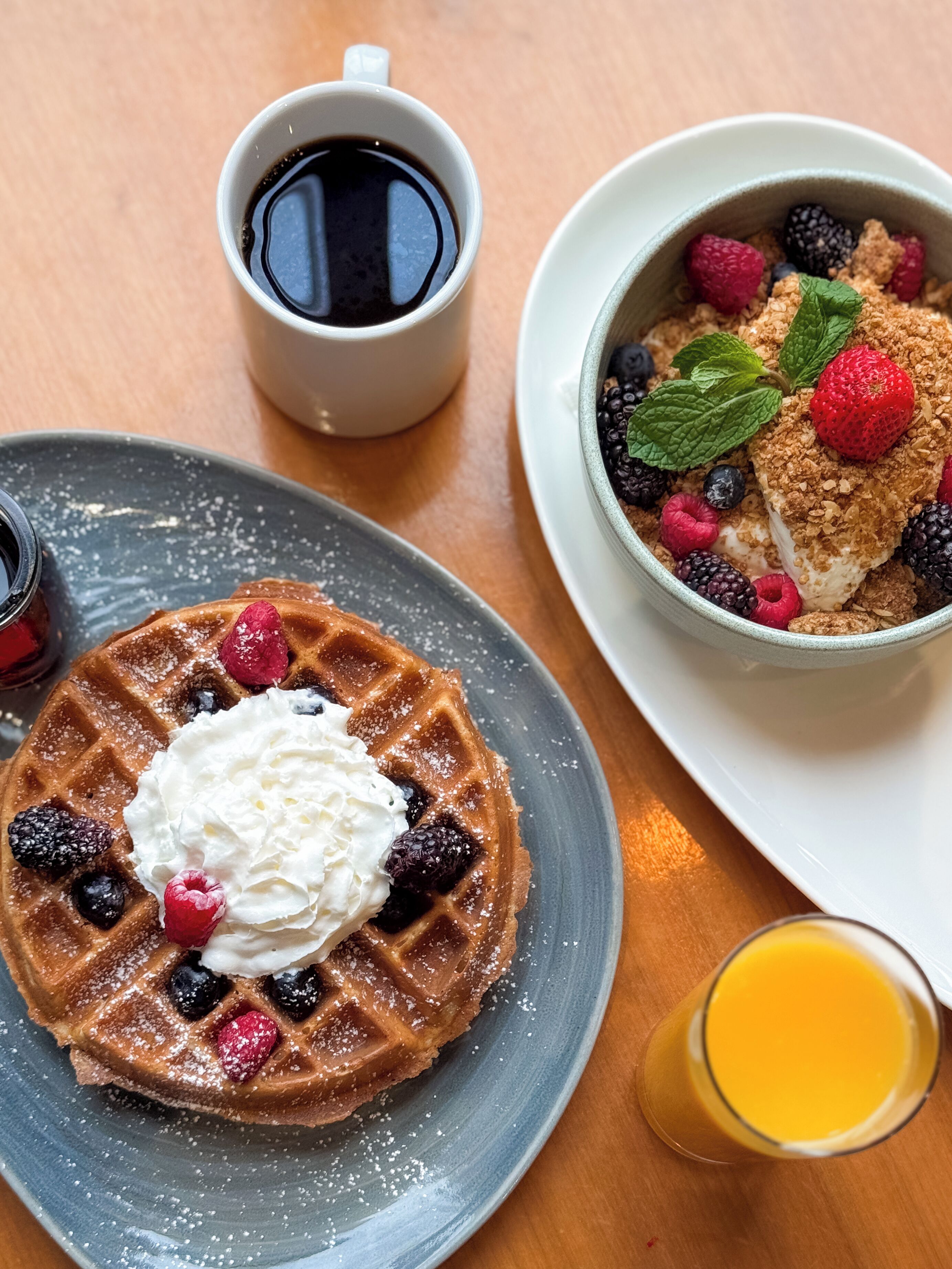 A breakfast setting with a waffle, berries, whipped cream, and a cup of coffee.