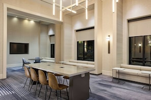 A modern hotel room with a large rectangular table, multiple chairs, a sofa, and a television.