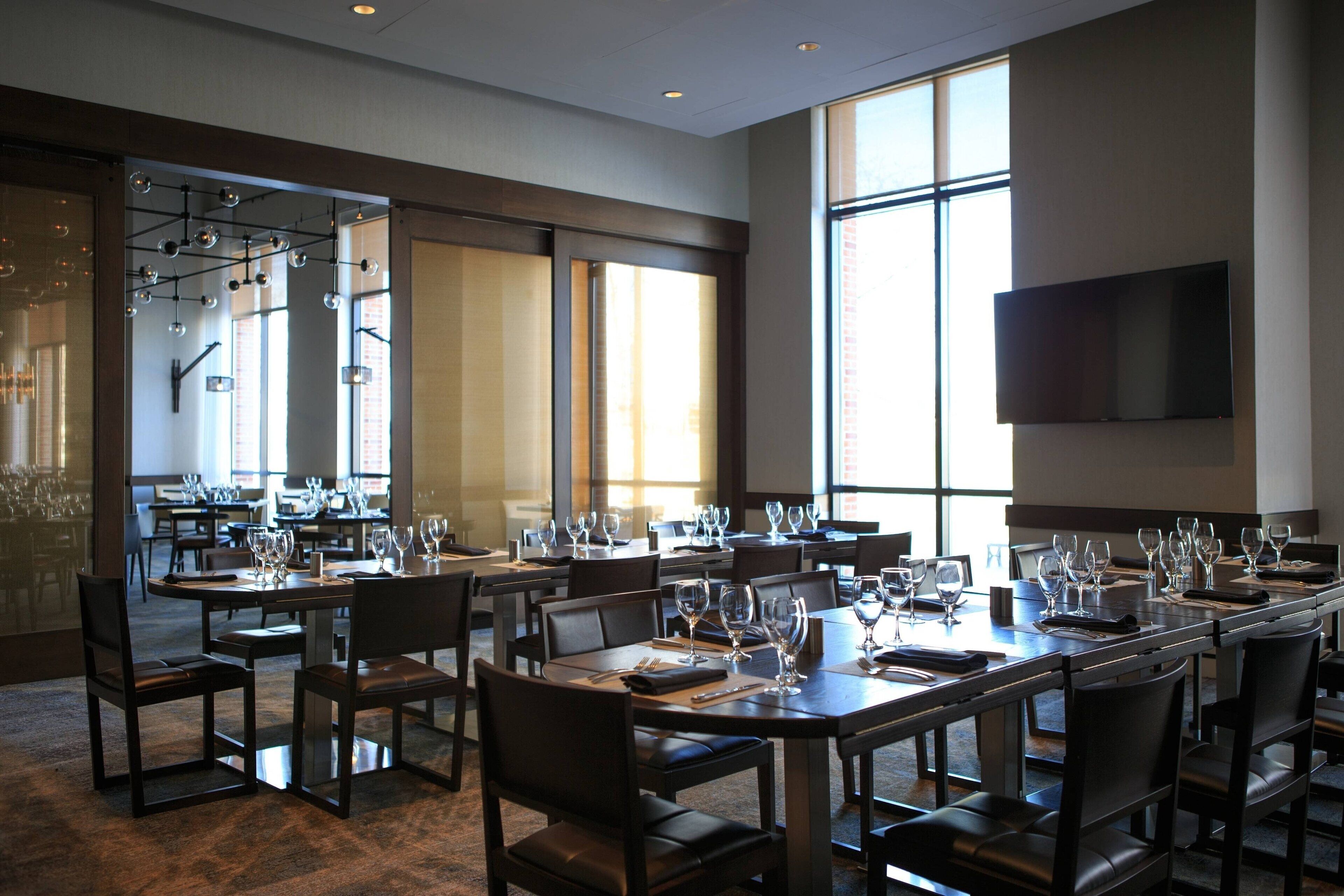 A large dining area with multiple tables set for a banquet, large windows, and a flat-screen TV mounted on the wall.