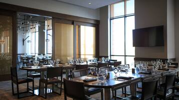 A large dining area with multiple tables set for a banquet, large windows, and a flat-screen TV mounted on the wall.