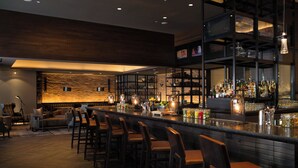 Una zona de bar moderna con una barra alargada, taburetes y estantes llenos de botellas.