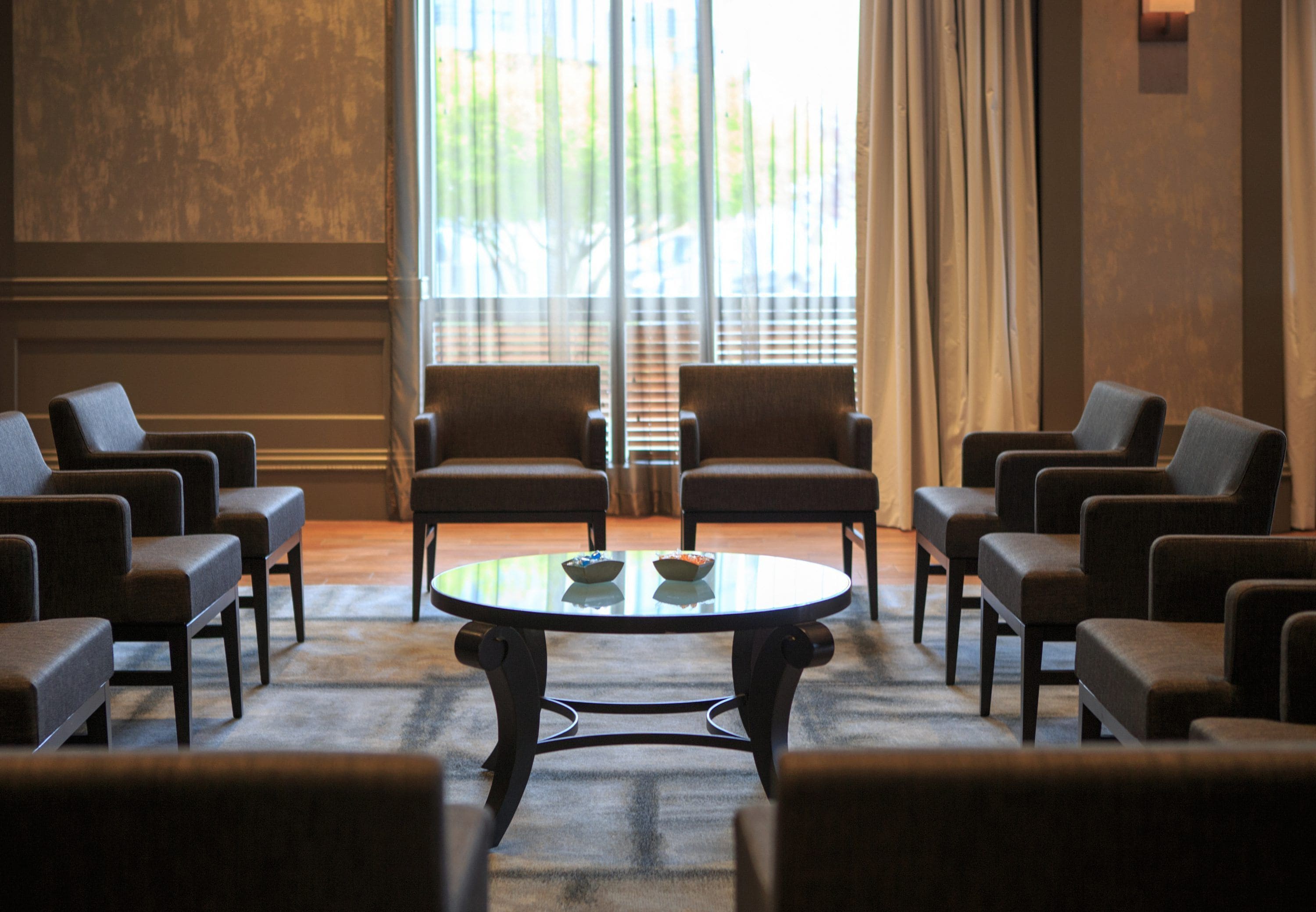 A conference room with a round table, multiple chairs, and a view through large windows.