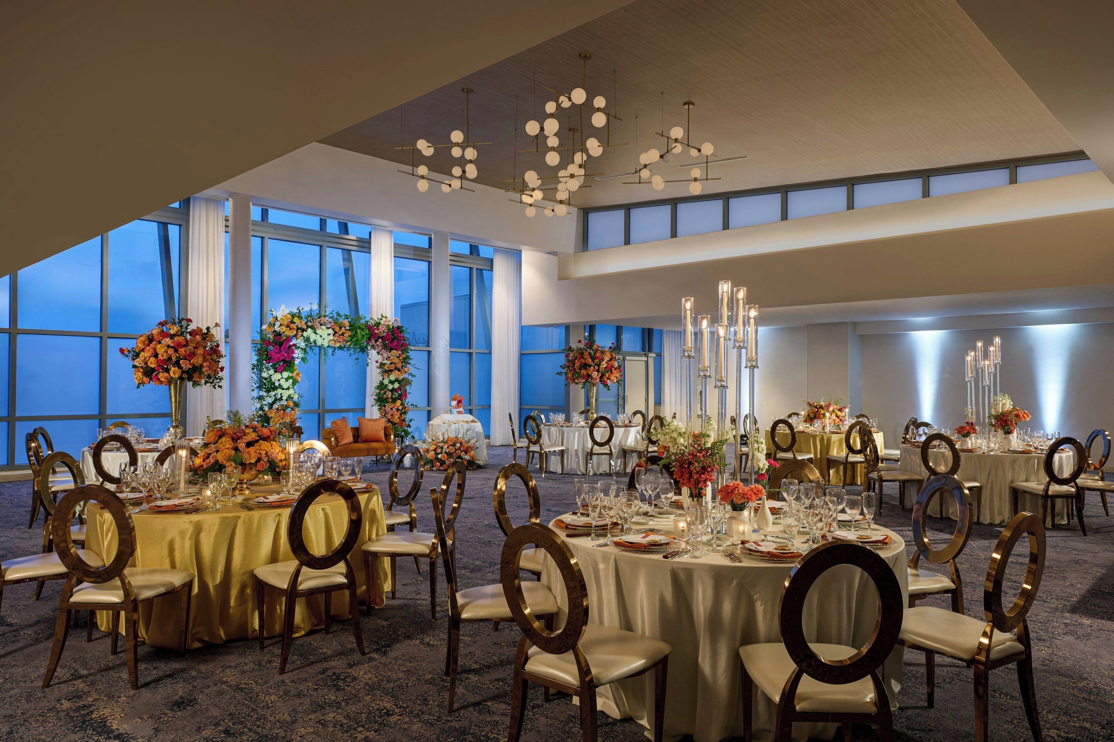 A banquet hall with round tables, gold tablecloths, and floral centerpieces.