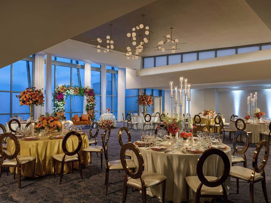 A banquet hall with round tables, gold tablecloths, and floral centerpieces.