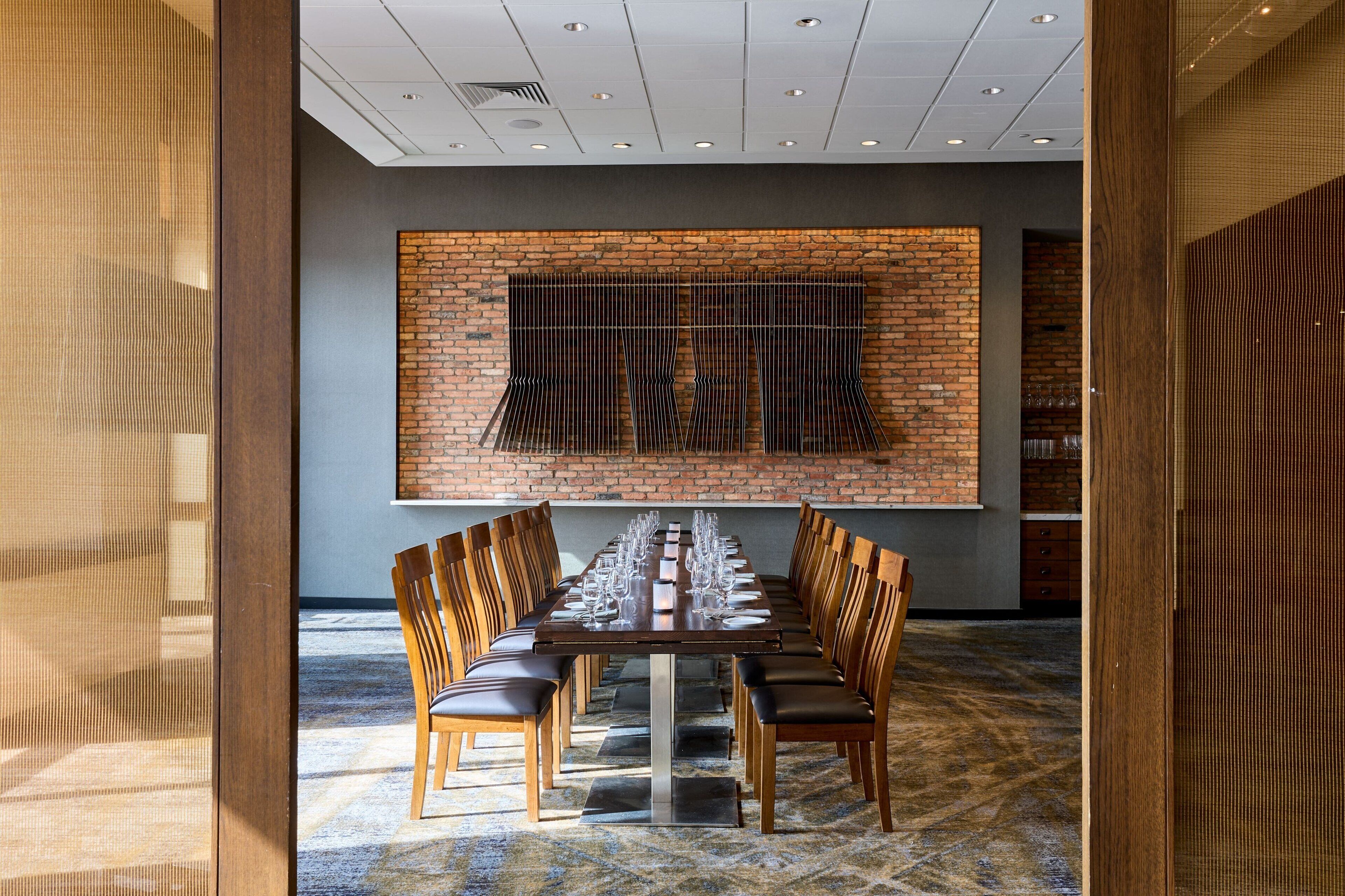 A long dining table with chairs, a brick wall, and a ceiling with recessed lighting.