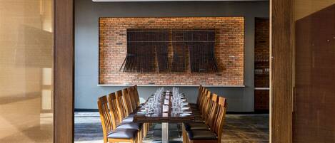 A long dining table with chairs, a brick wall, and a ceiling with recessed lighting.