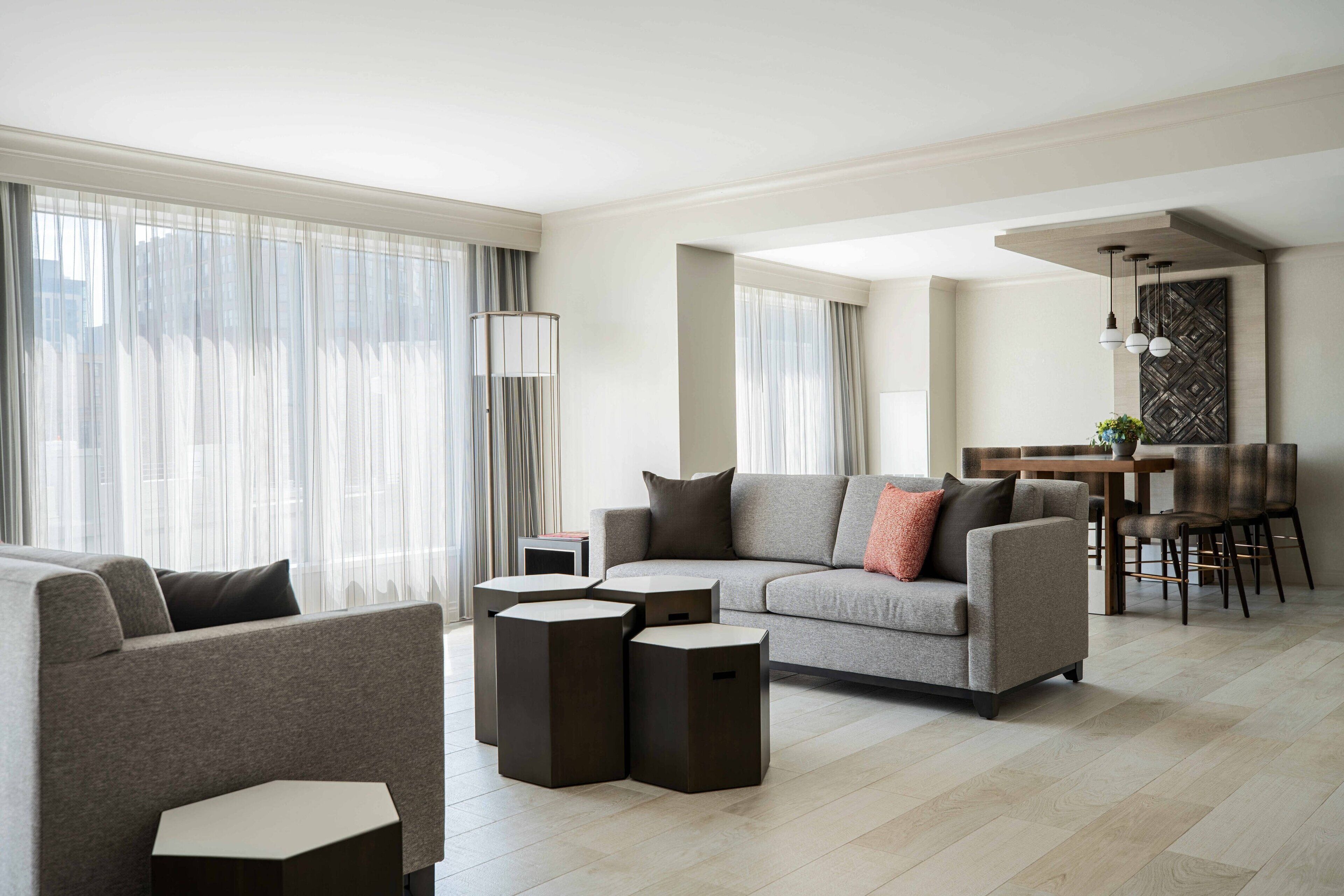 A modern living room with a grey sofa, a coffee table, and a dining area with chairs and a table.
