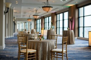 A banquet hall with round tables, chairs, and hanging lamps.
