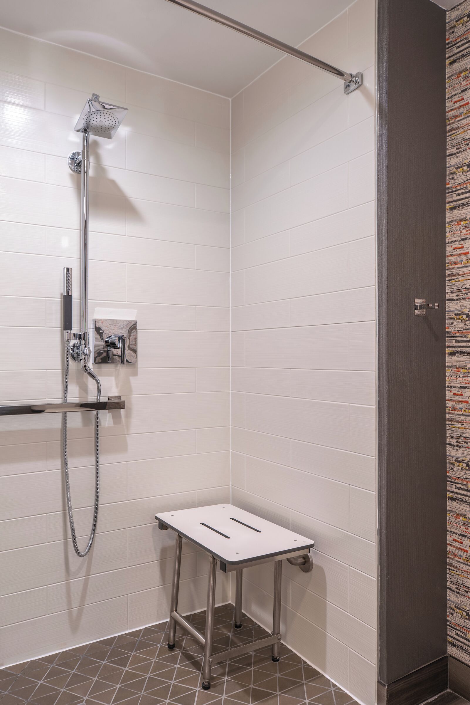 Zona de ducha con cabezal de ducha de mano, panel de control en la pared y una pequeña mesa.
