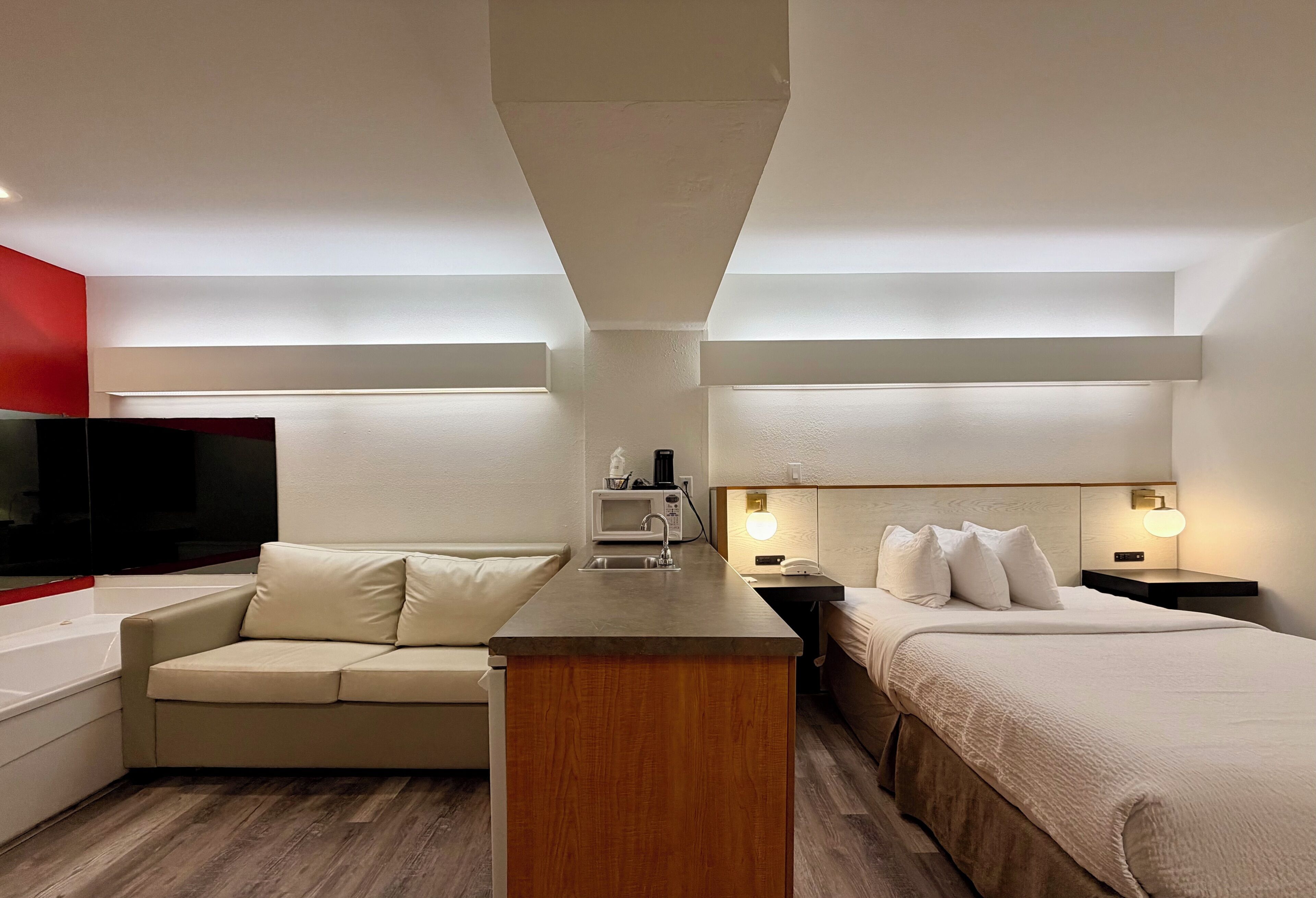A hotel room with a kitchenette, a sofa, a bed, and a TV.