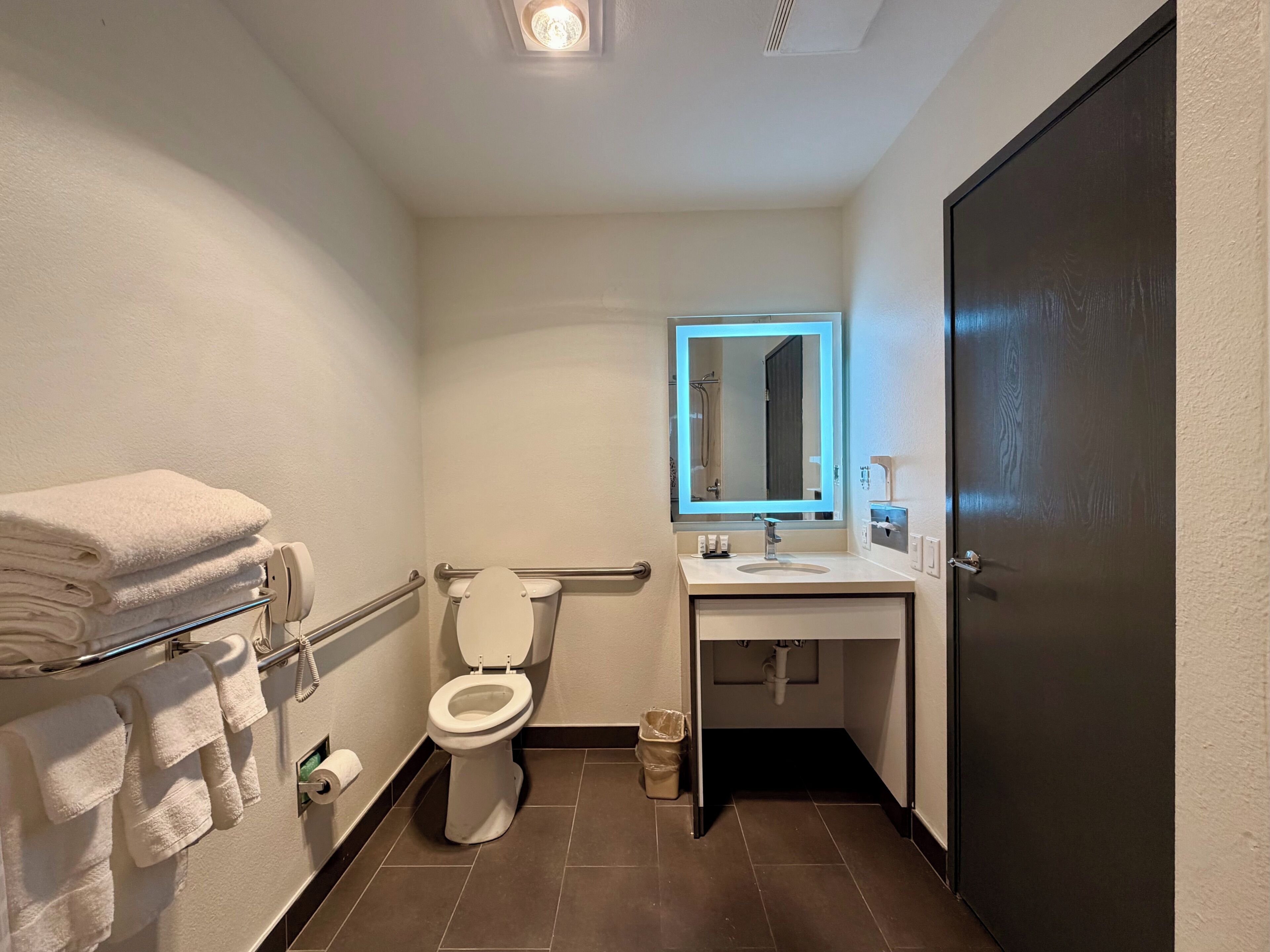 A bathroom with a toilet, a sink, a mirror, a towel rack, and a door.