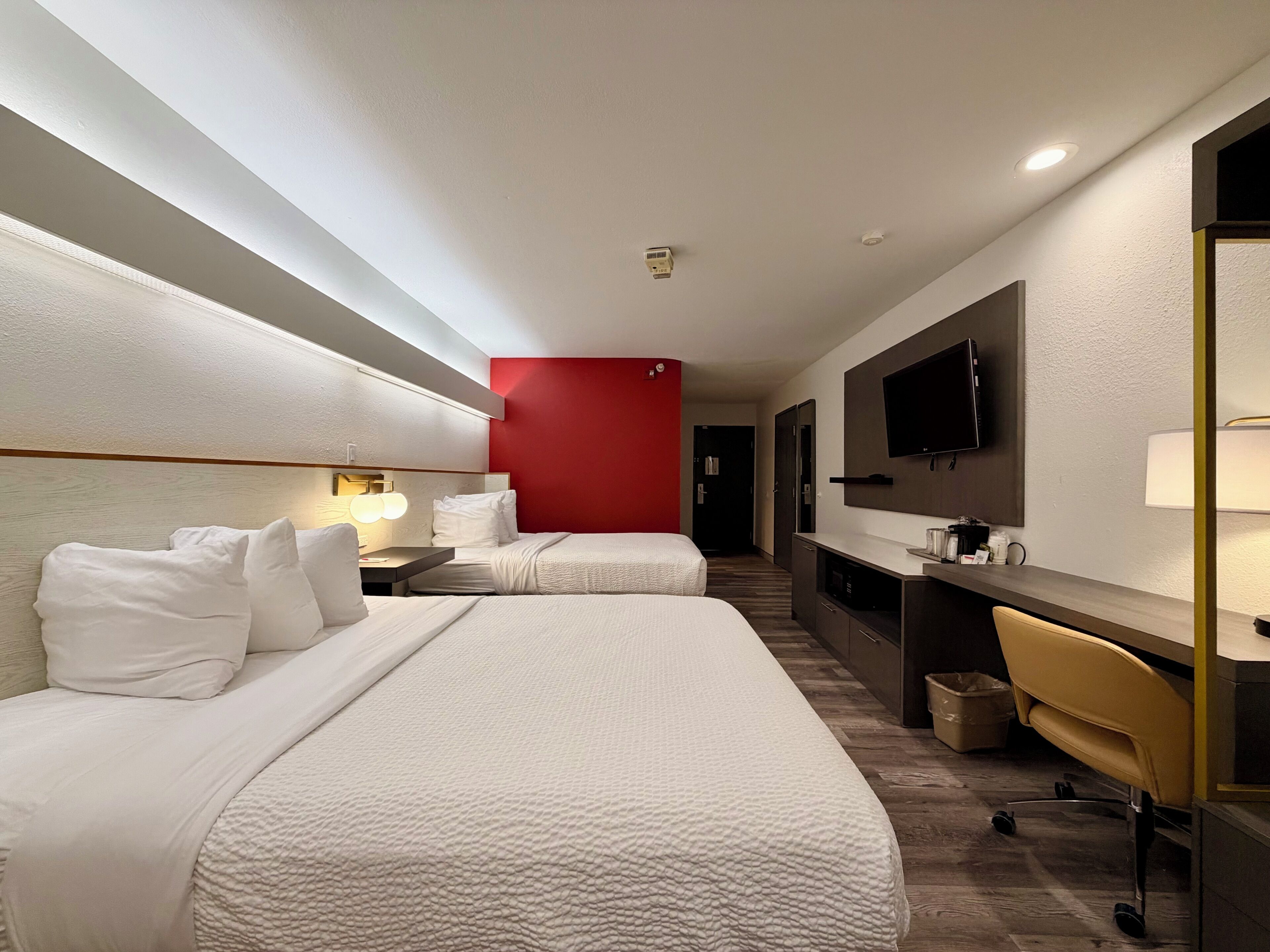 Ein Hotelzimmer mit zwei Betten, einem Schreibtisch, einem Stuhl, einem Fernseher und einer Wand in roter Farbe.