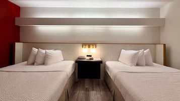 A hotel room with two beds, a bedside table with a lamp, and a red accent wall.