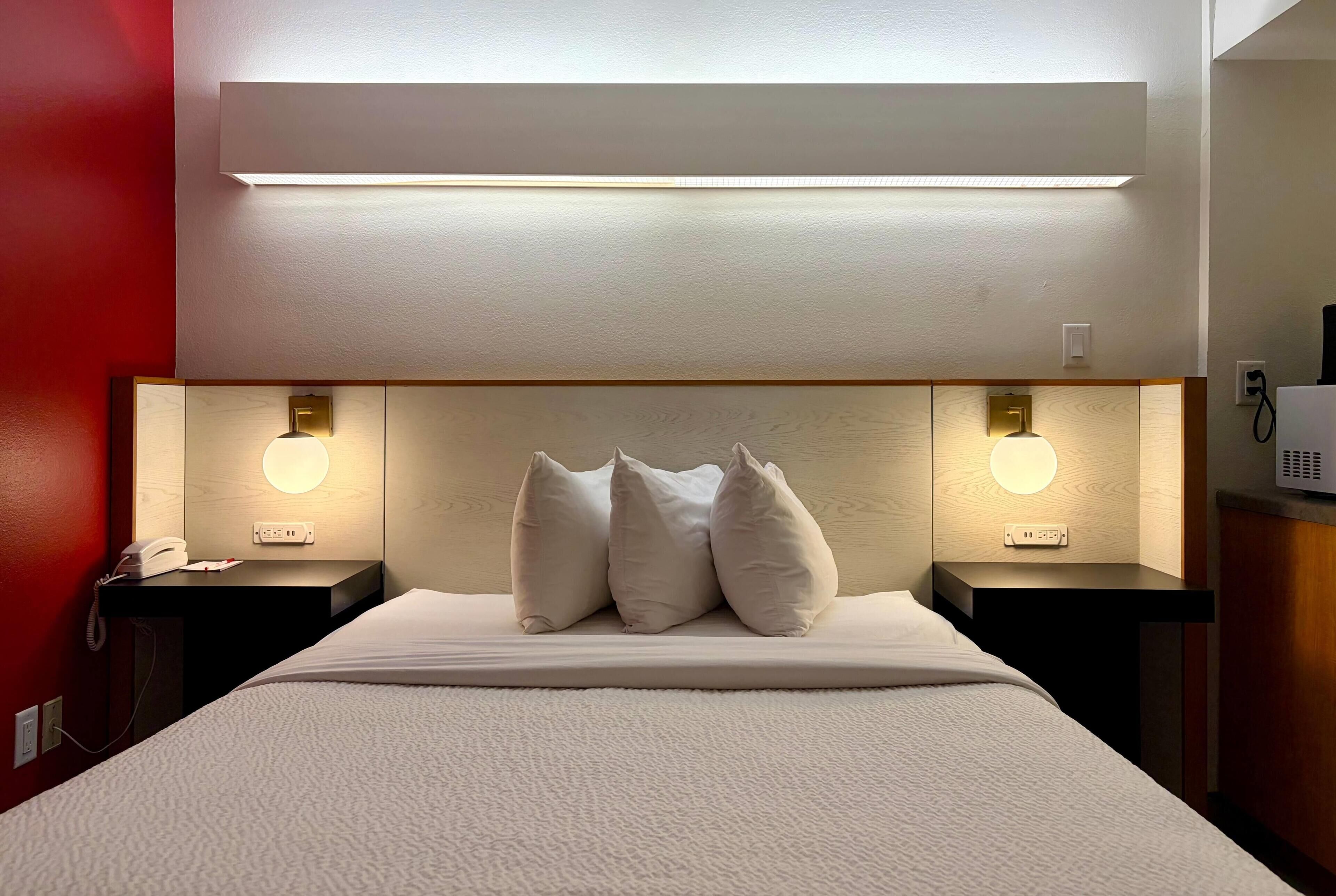 A hotel room with a bed, bedside lamps, a telephone, and a wall-mounted light fixture.
