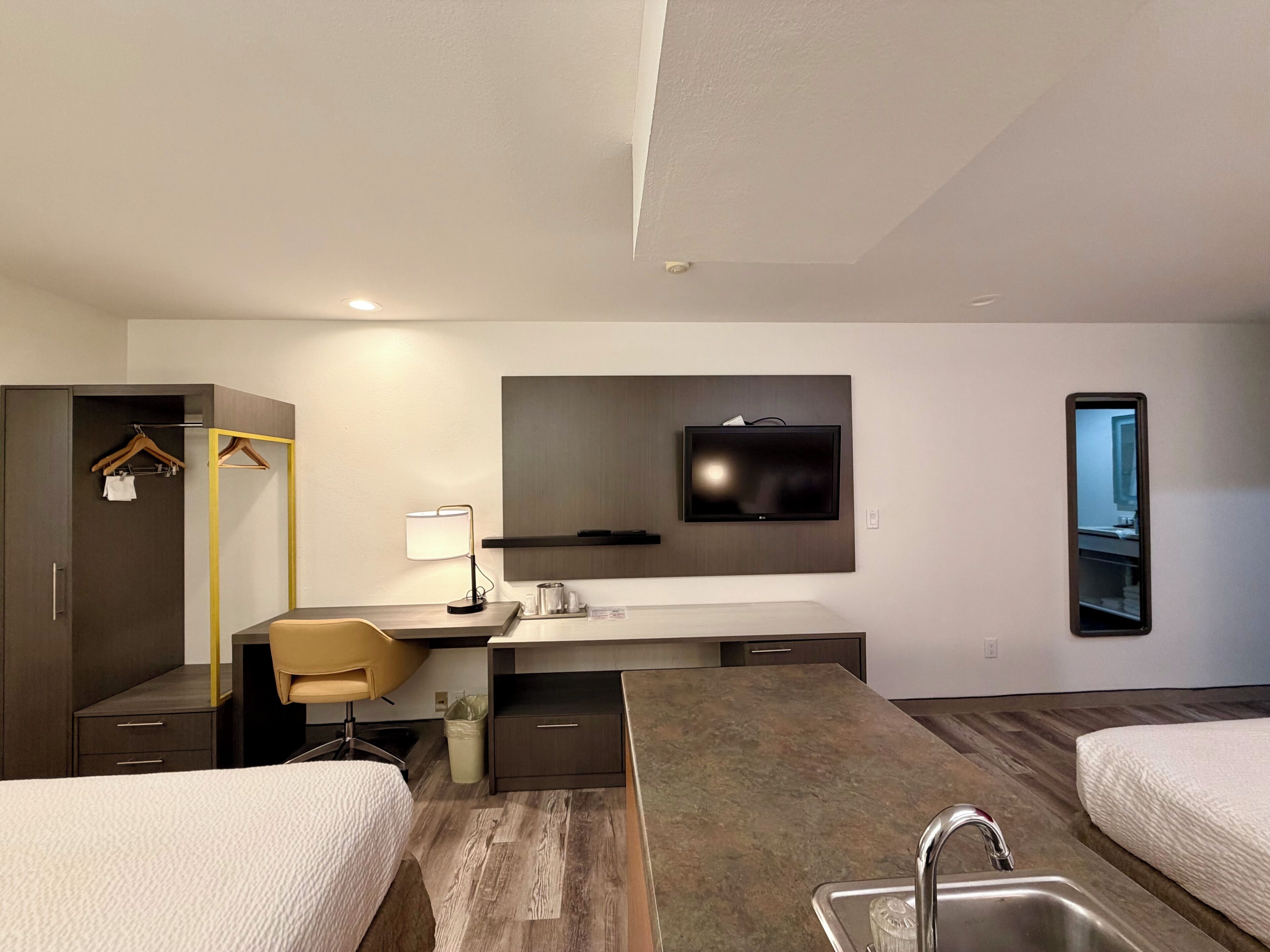 Una habitación de hotel con cama, escritorio, televisor, espejo y baño.