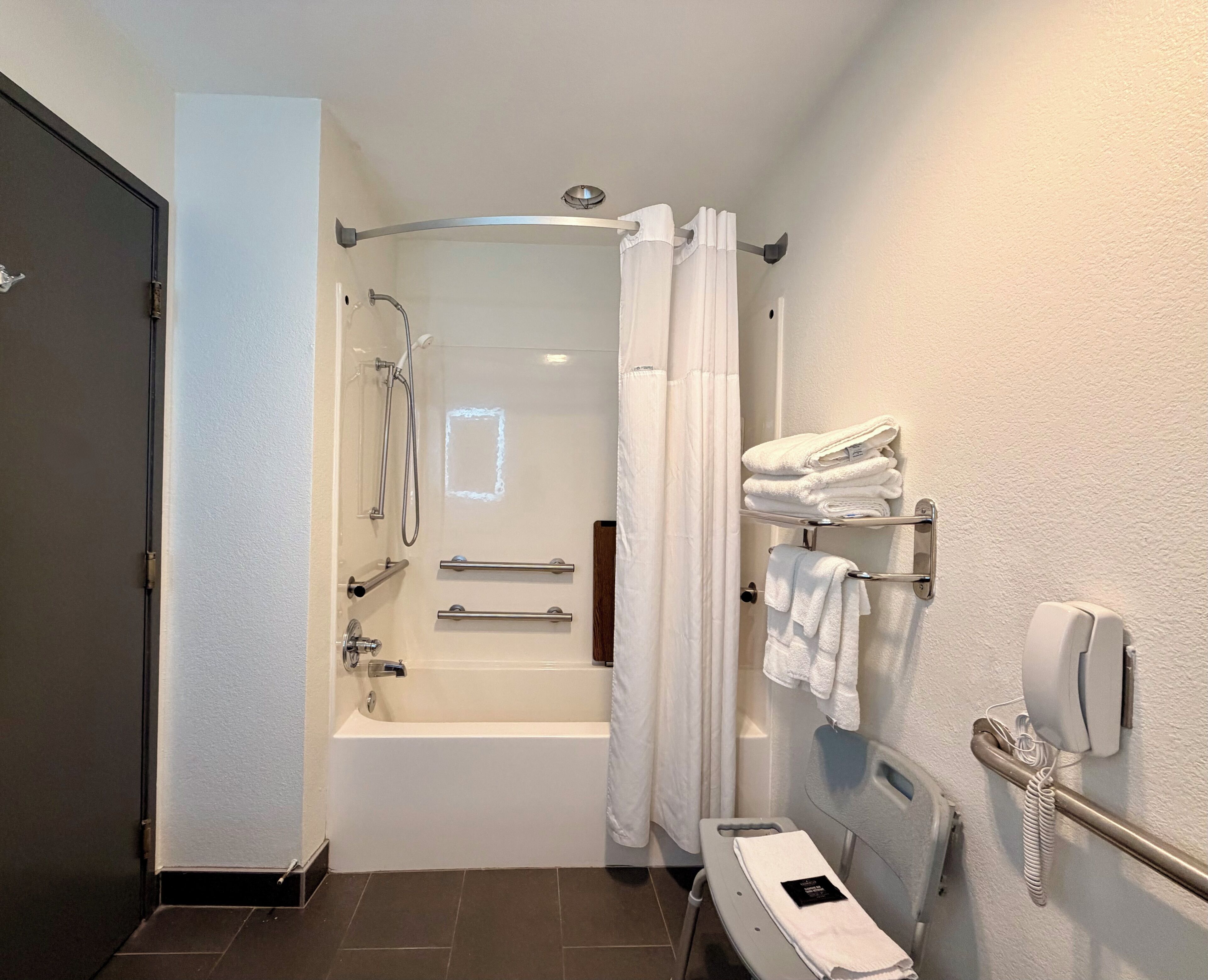 A modern bathroom with a bathtub, shower, and toilet. There are towels and a phone on the wall.