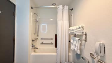 A modern bathroom with a bathtub, shower, and toilet. There are towels and a phone on the wall.