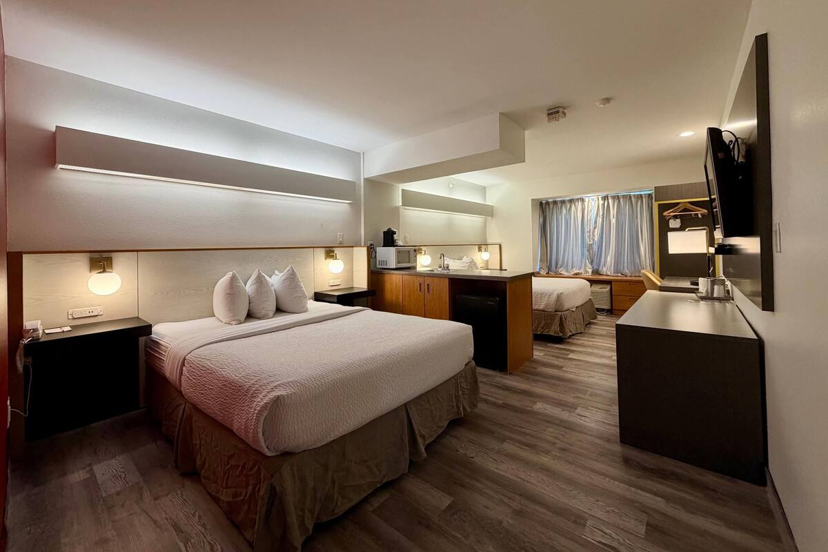 A hotel room with a large bed, a desk, a microwave, a TV, and a separate sleeping area.