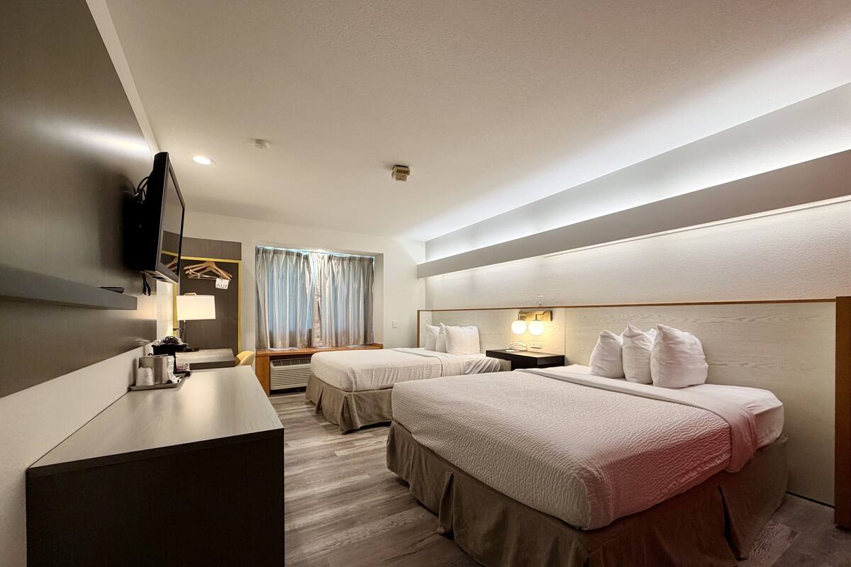 A hotel room with two beds, a desk, a TV, and a window with curtains.