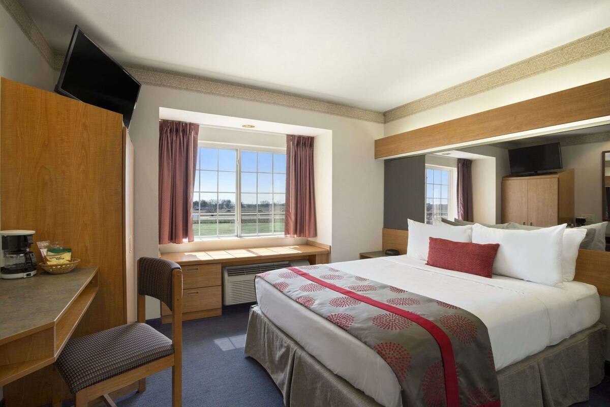 A hotel room with a bed, desk, chair, and a window with curtains.