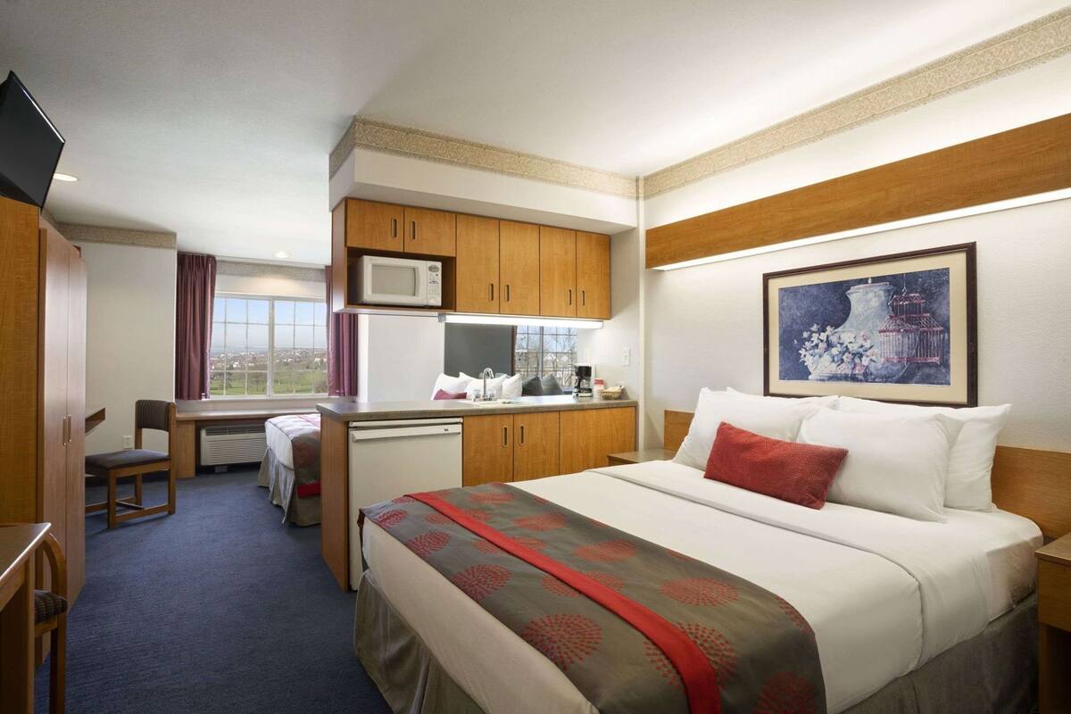 A hotel room with a bed, a desk, a microwave, a sink, and a window with a view.