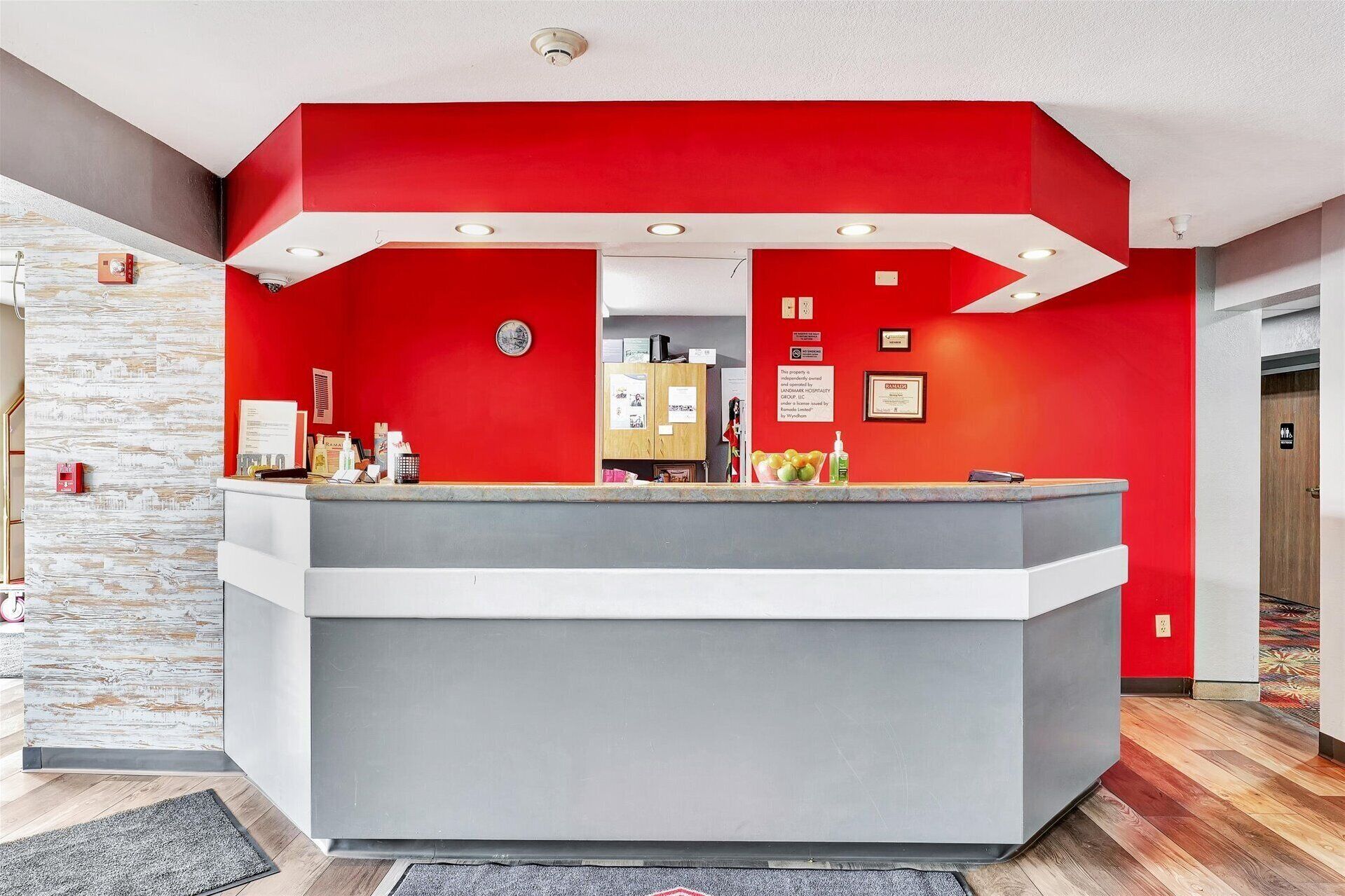 Ein Empfangsbereich mit roter Akzentwand, grauem Empfangstresen und einer Steinsäule links.