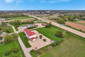 An aerial view of a building with a red roof, surrounded by green fields and a highway. - Ramada Limited Bloomington IL I-74/I-55 (Bloomington)