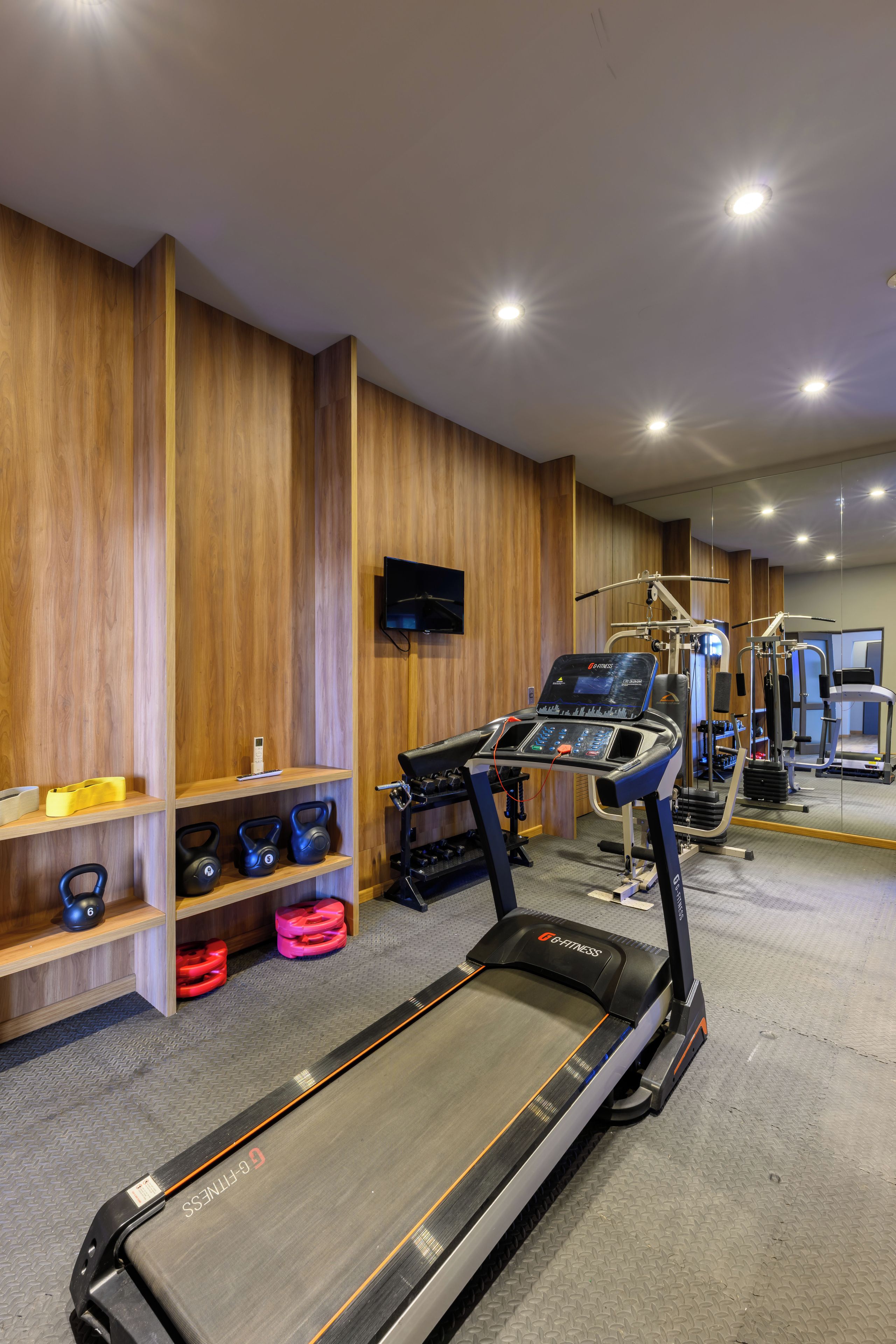 Une salle de sport équipée de tapis de course, d’appareils de musculation et de kettlebells.