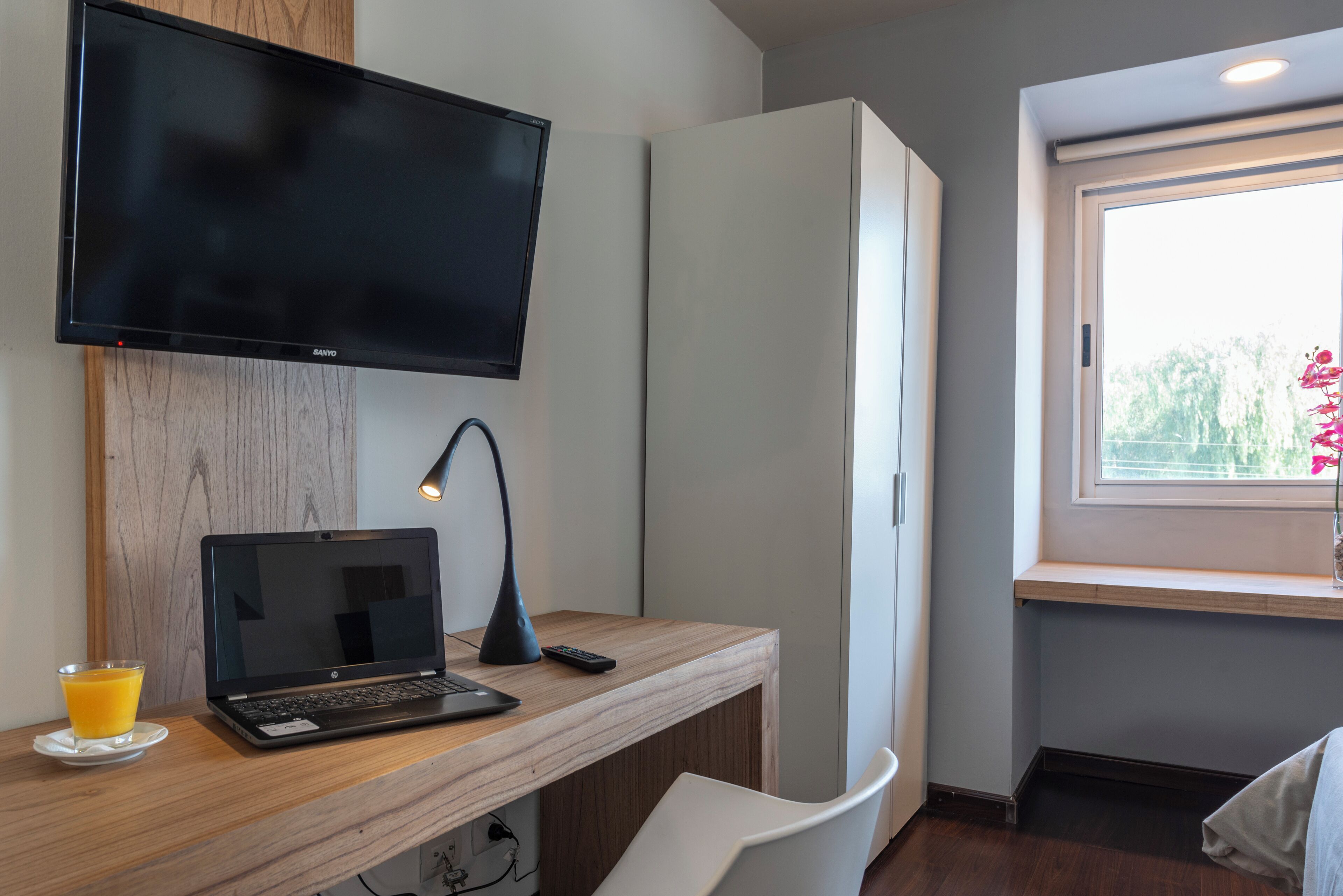 A modern room with a wooden desk, a laptop, a remote, and a glass of orange juice.