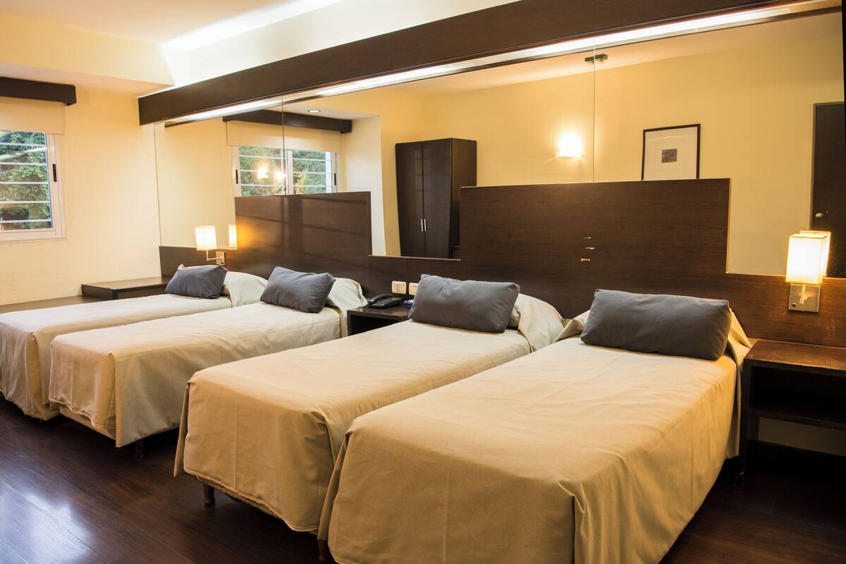 A hotel room with two single beds, a large mirror, a wardrobe, and bedside lamps.