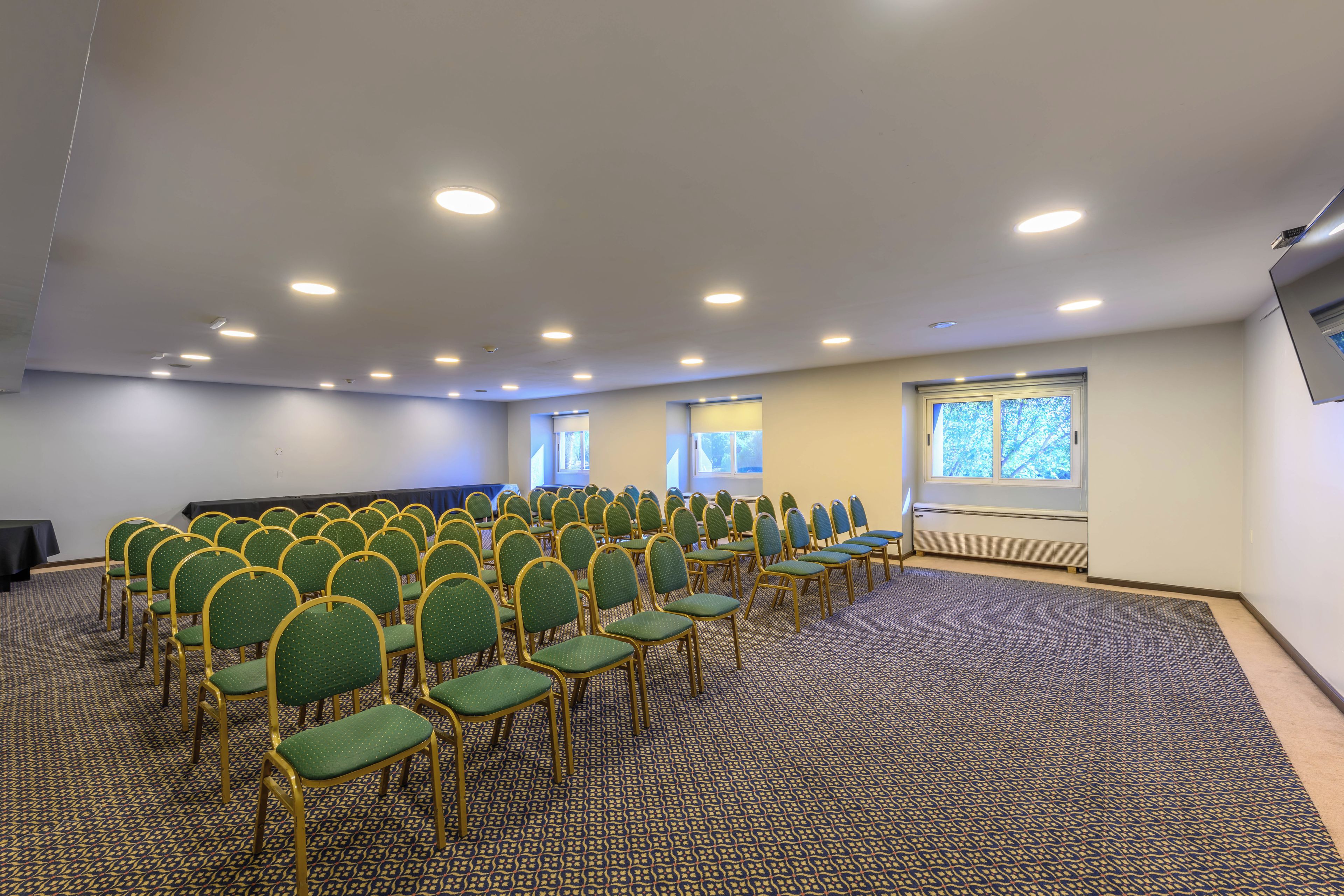 Une salle de conférence avec des rangées de chaises, un sol recouvert de moquette et un plafond doté d’un éclairage encastré.