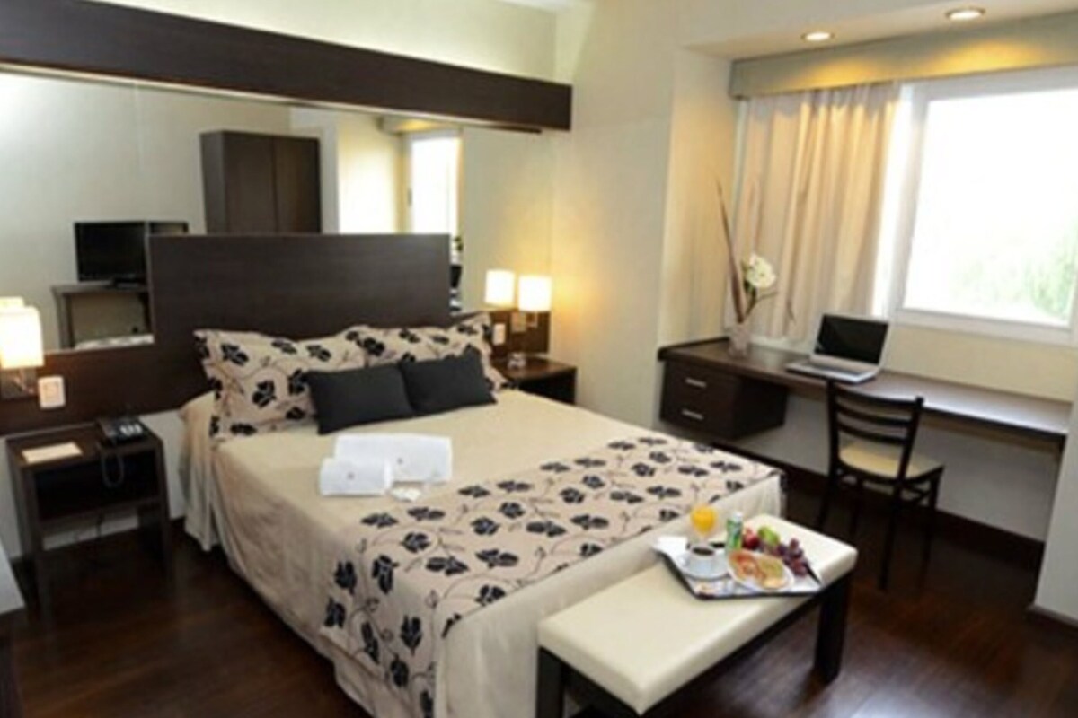 A hotel room with a bed, bedside tables, a desk, a chair, a laptop, and a breakfast tray.