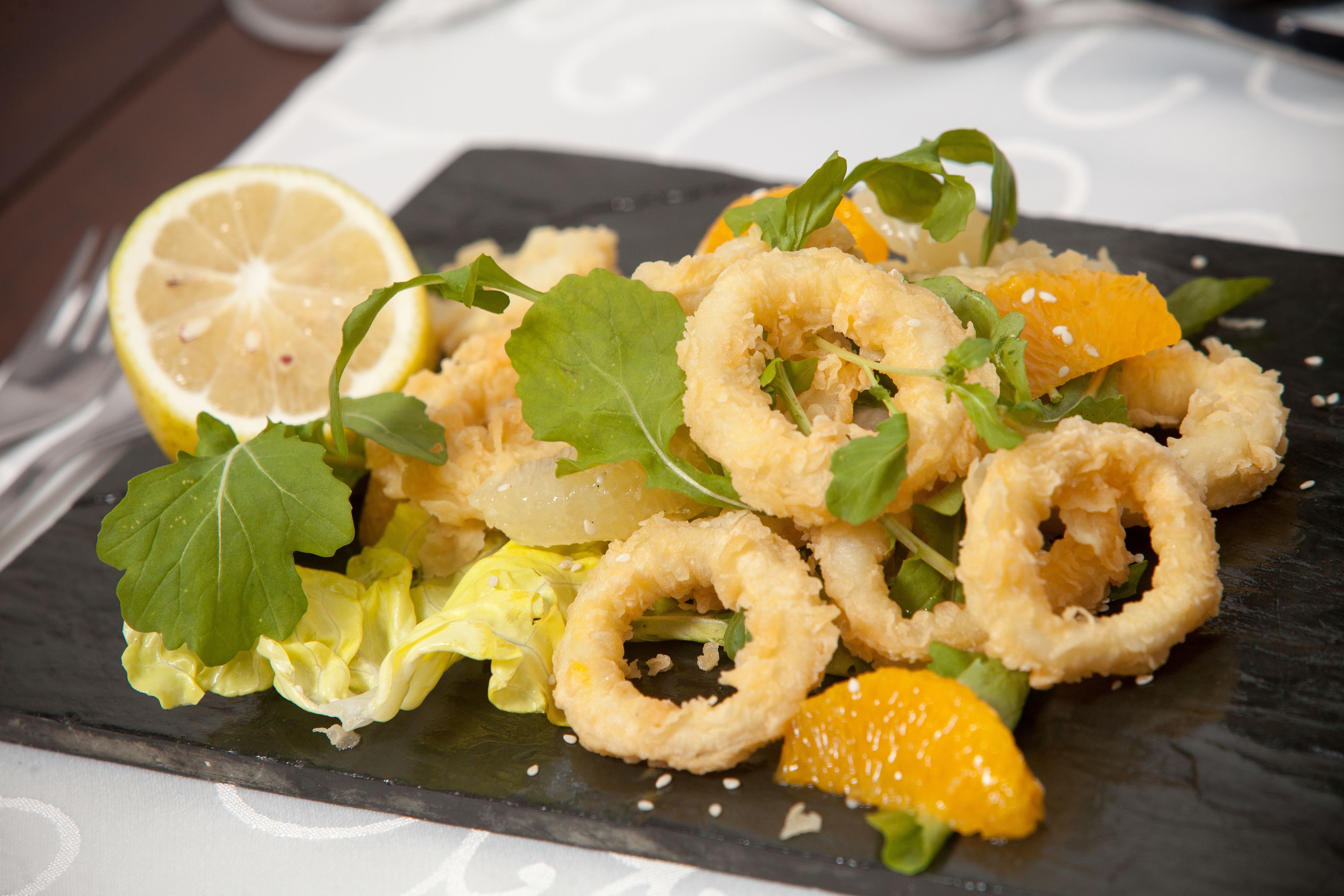Un plato de comida con aros de calamares fritos, segmentos de naranja y verduras de hoja verde.