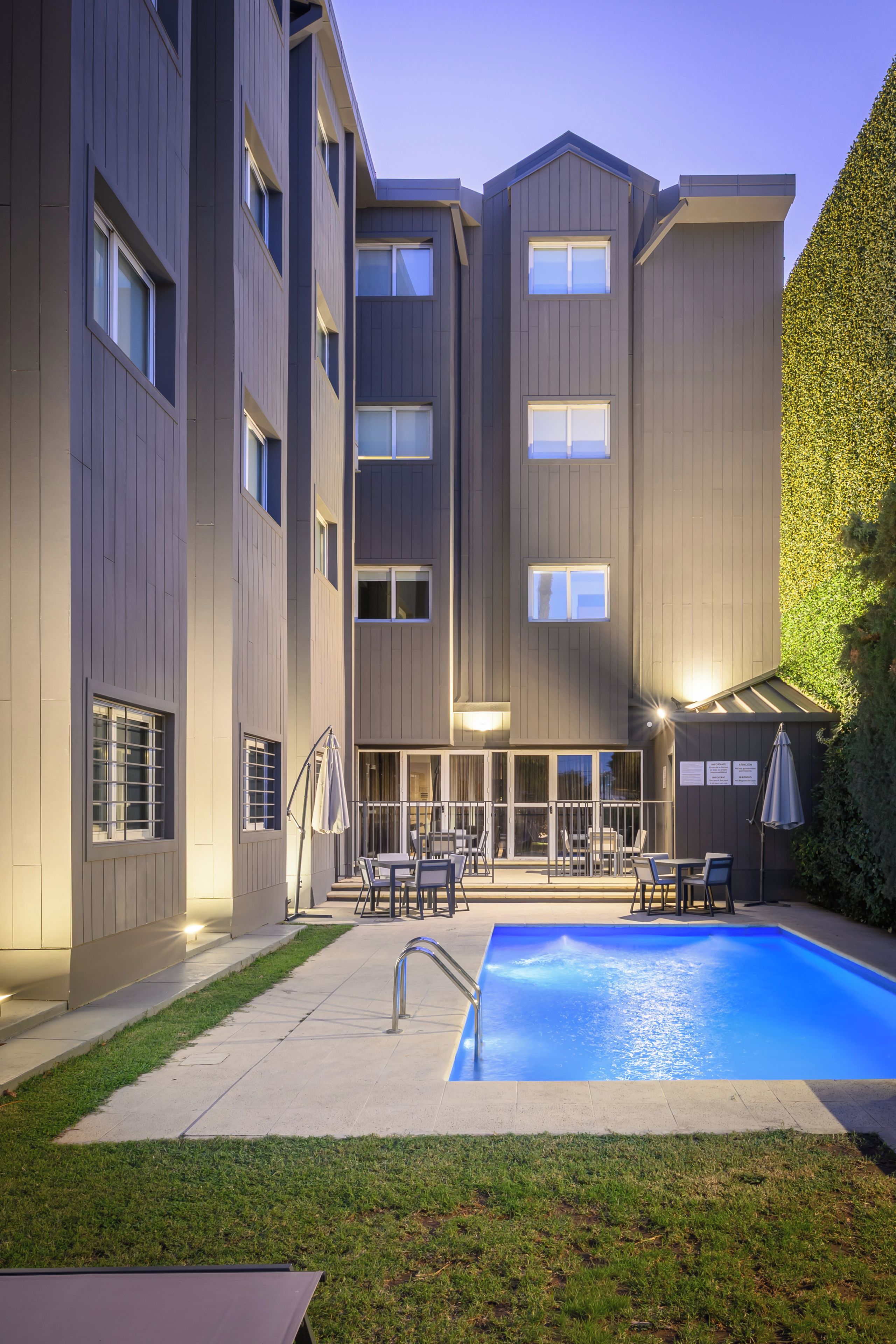 Un edificio moderno con piscina, mobiliario exterior y un césped bien cuidado.