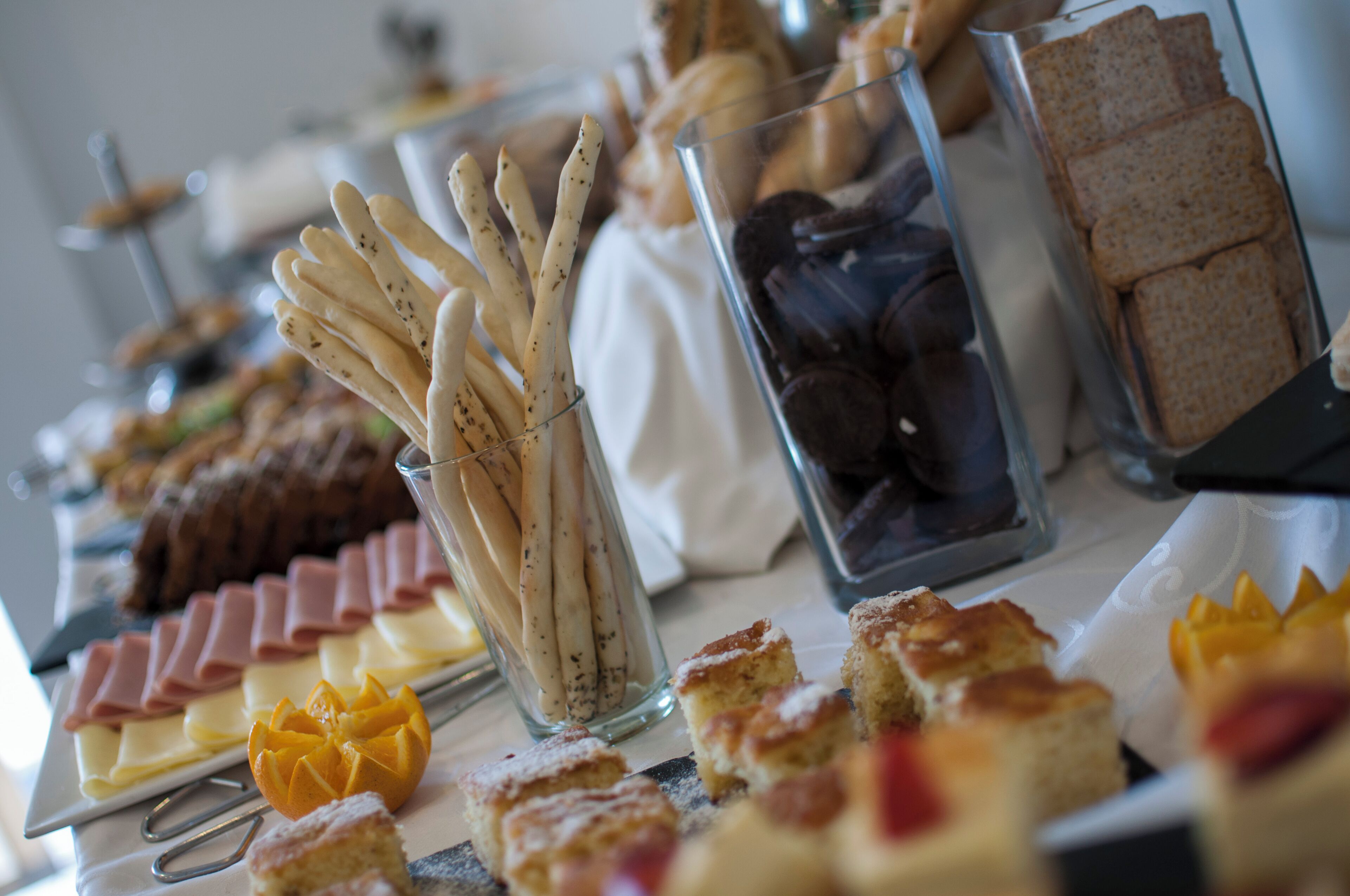 Uma mesa de buffet com diversos alimentos, incluindo palitos de pão, doces e sanduíches.
