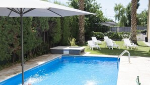 Une piscine avec un parasol, des chaises longues et un petit coin jardin.