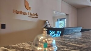 Un espace d’accueil d’hôtel avec une cloison en verre, un comptoir d’accueil et une cloche.