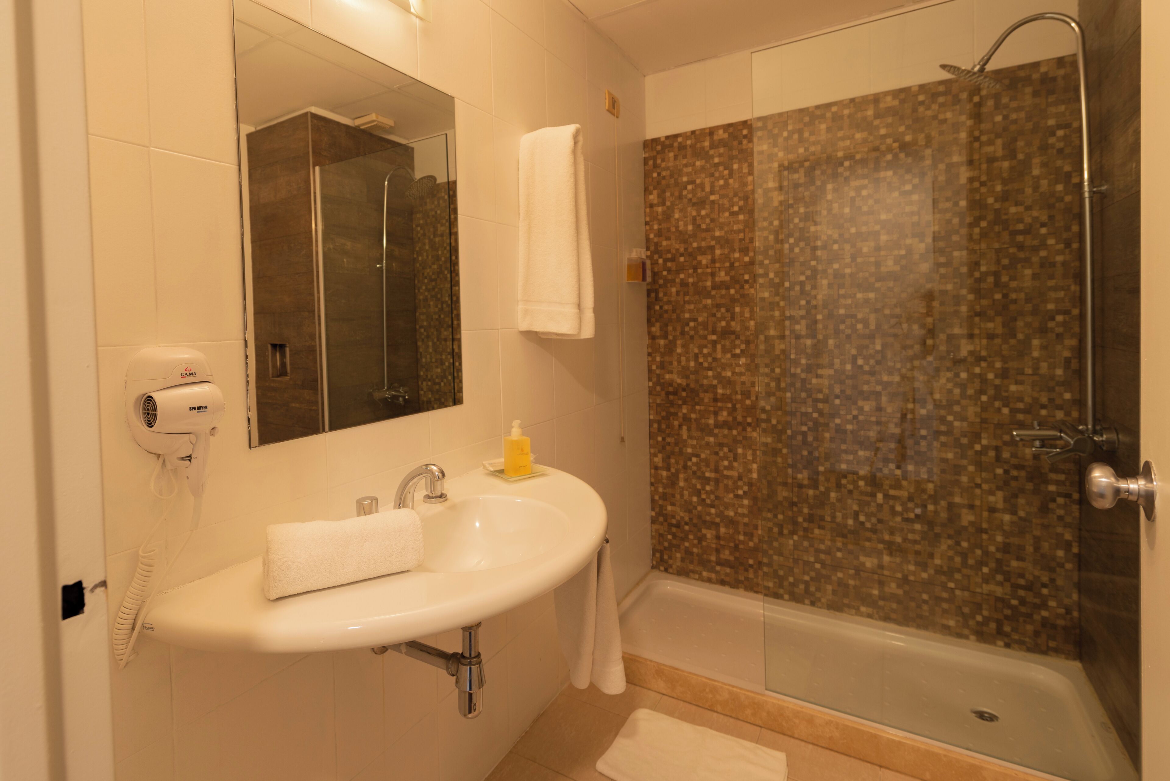 A bathroom with a sink, mirror, towel rack, and shower with mosaic tiles.