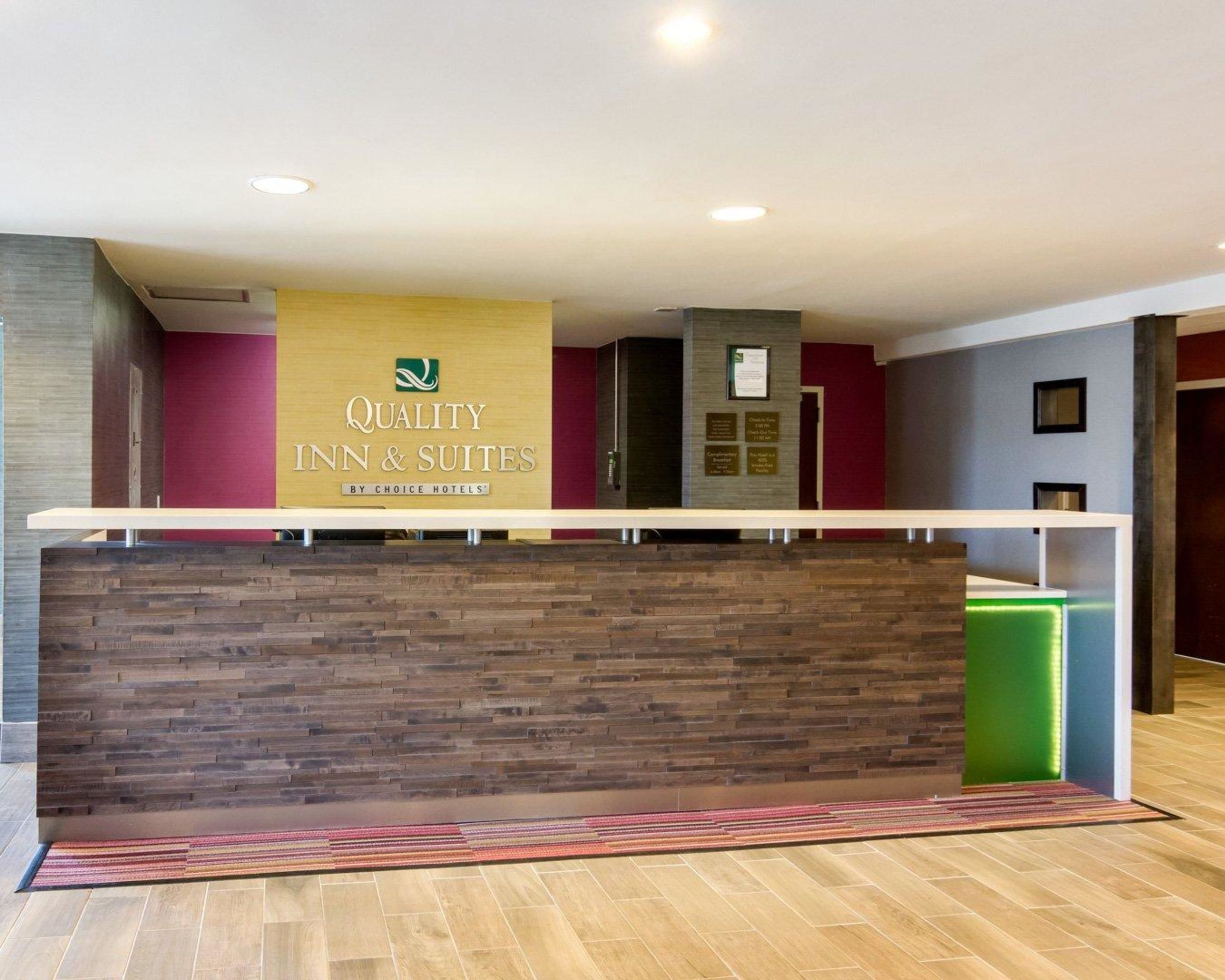 Un mostrador de recepción con diseño de panel de madera, un letrero de Quality Inn & Suites by Choice Hotels, y un bote de basura verde a la derecha.