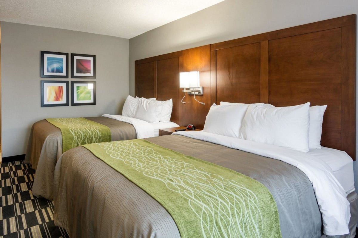 A hotel room with two beds, a wooden headboard, a wall-mounted lamp, and framed pictures.