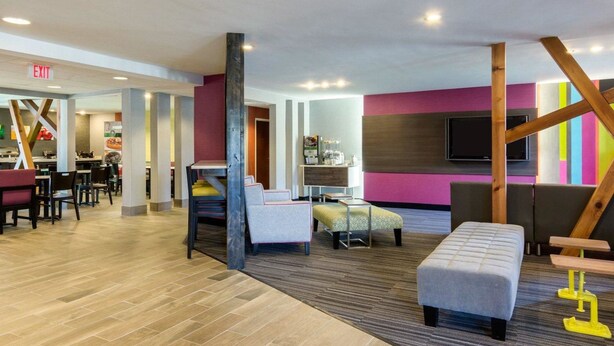 A modern hotel lobby with a dining area, a seating area with a sofa and ottoman, and a TV mounted on the wall. - Quality Inn & Suites Ashland near Kings Dominion (Ashland)