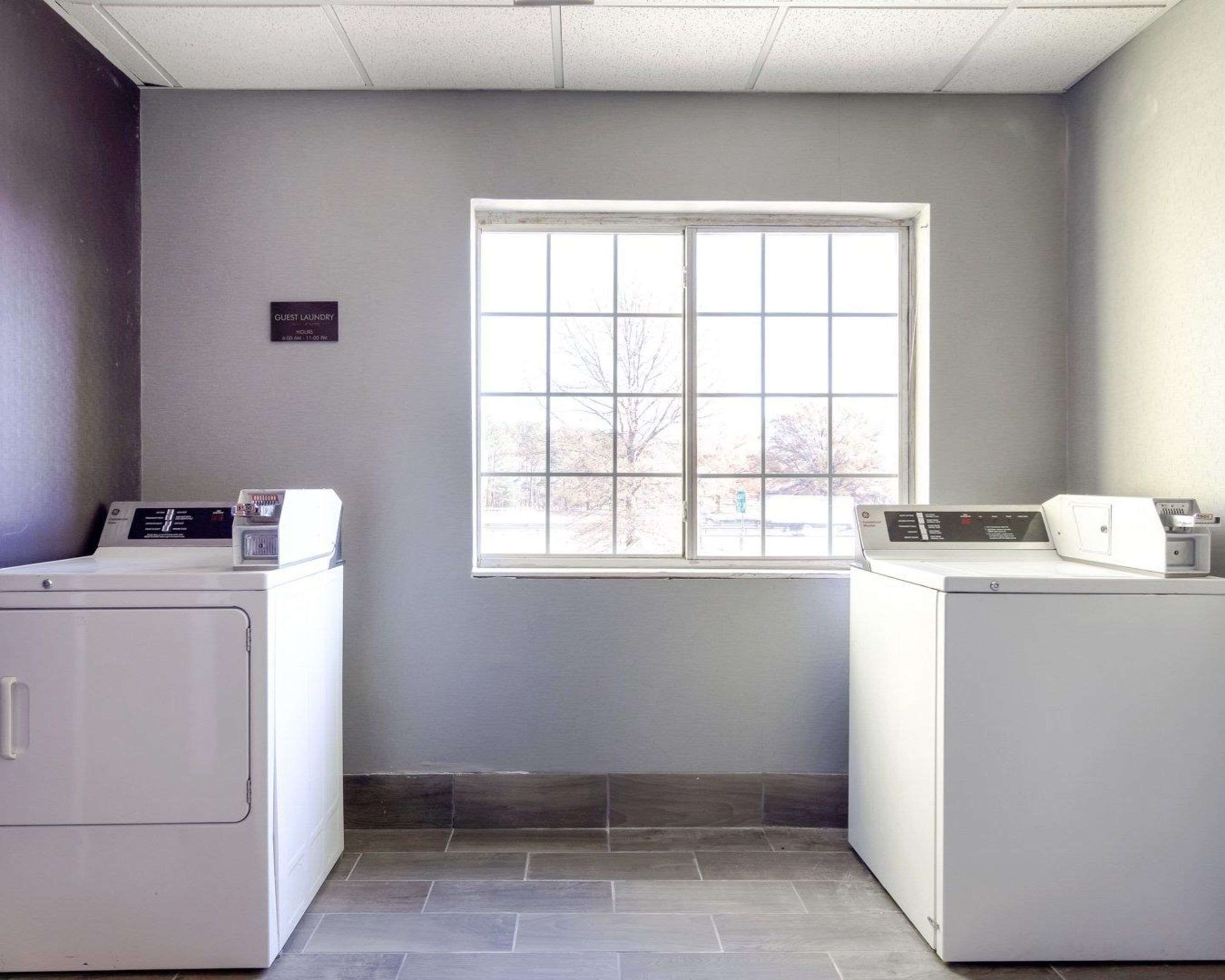 A laundry room with two washing machines, a window, and a sign indicating guest laundry hours.