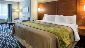 A hotel room with a large bed, a desk, a chair, a window with curtains, and a wall-mounted lamp. - Quality Inn & Suites Ashland near Kings Dominion (Ashland)