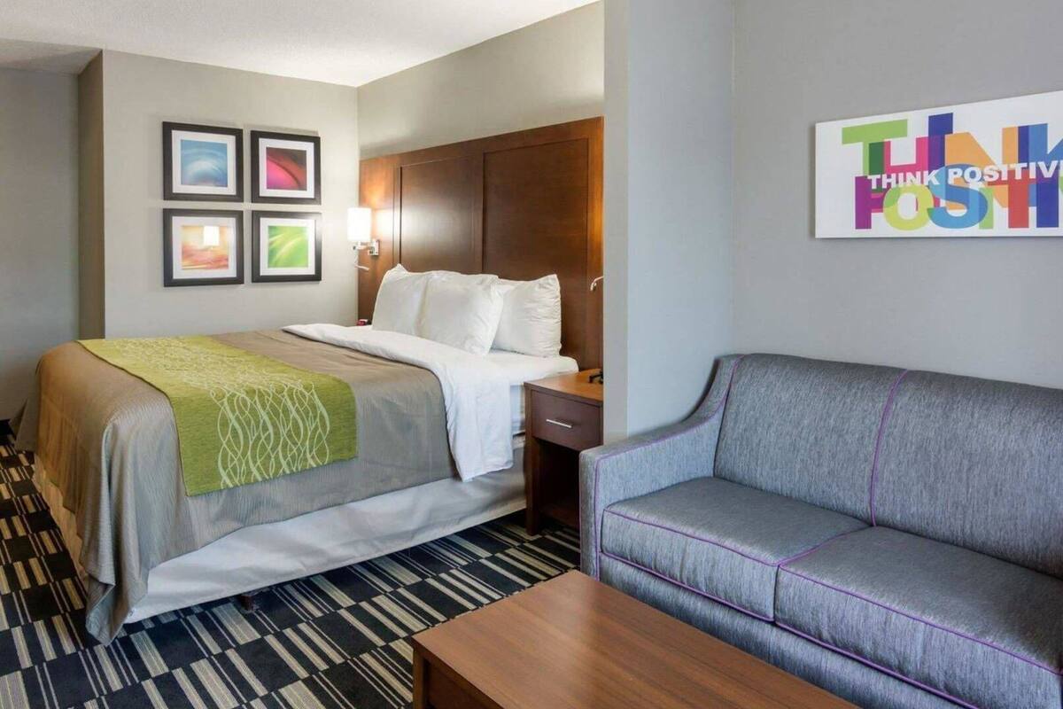 A hotel room with a bed, a sofa, a wall with framed pictures, and a motivational poster.