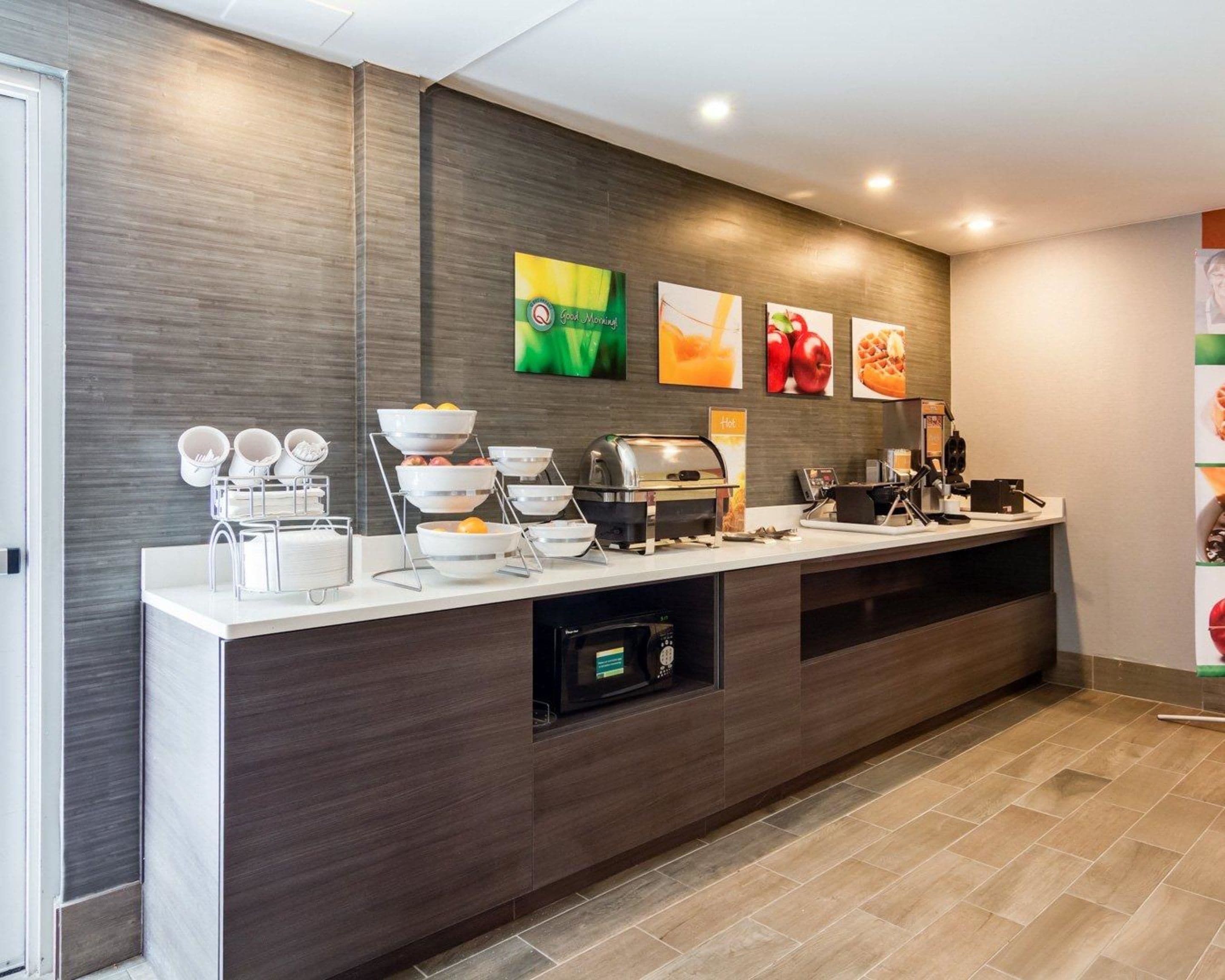 Zona de recepción moderna de un hotel, con una barra para desayunos tipo buffet, una máquina de café y un microondas.