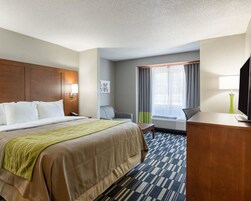 Habitación de hotel con una cama grande, un escritorio con lámpara, una silla, una ventana con cortinas y un televisor.