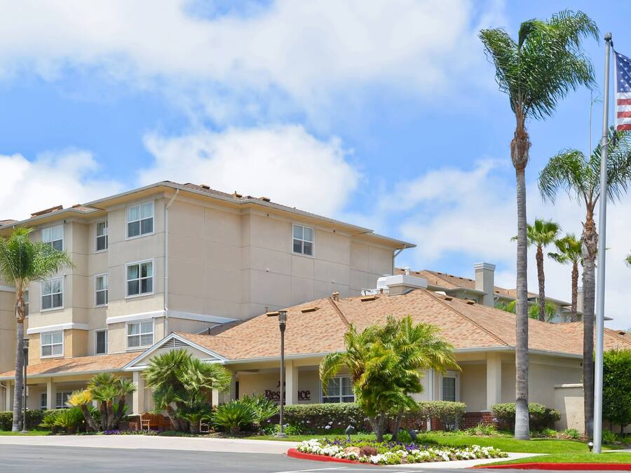 Un hotel de varios pisos con fachada color beige, palmeras y una bandera estadounidense.