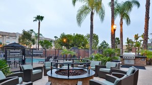 An outdoor patio area with wicker furniture, a fire pit, and a pool in the background. - Residence Inn by Marriott Los Angeles LAX/El Segundo (El Segundo)